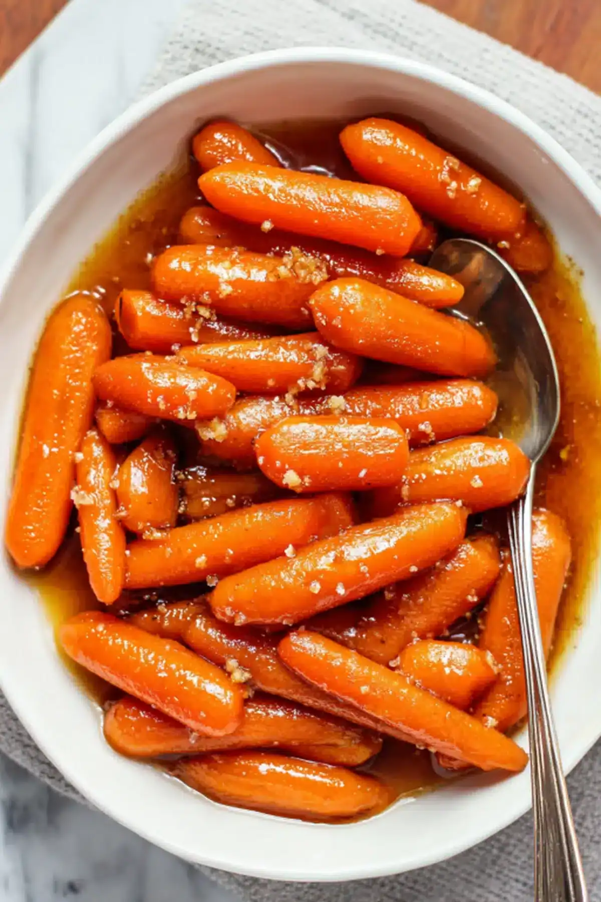Sweet glazed carrots in a white bowl with a spoon, ready for serving.